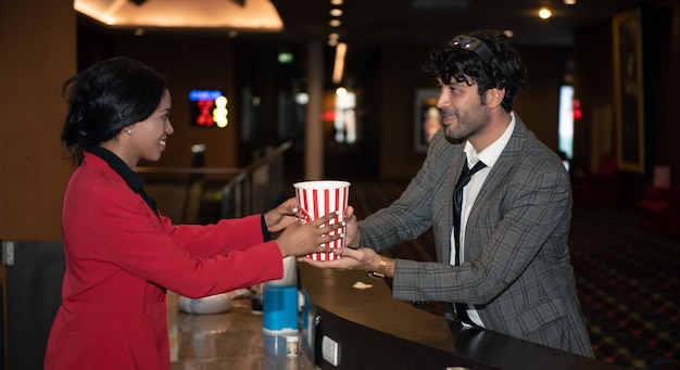 Young man buying popcorn snack at theatre shop counter.