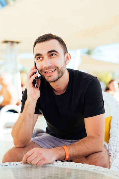 Young man calling by cell phone in outdoor cafe on summer resort at beach