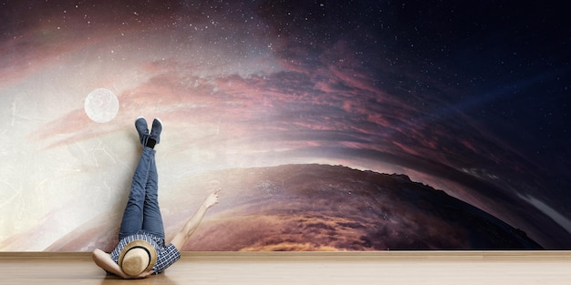 Young man in casual clothes and hat lying on the floor with legs raised up. Mixed media