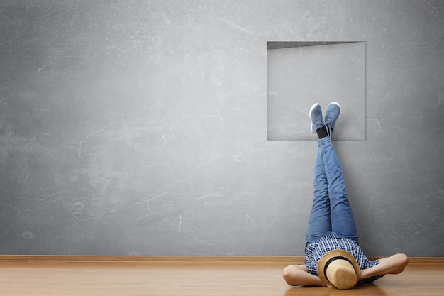 Young man in casual clothes and hat lying on the floor with legs raised up. Mixed media