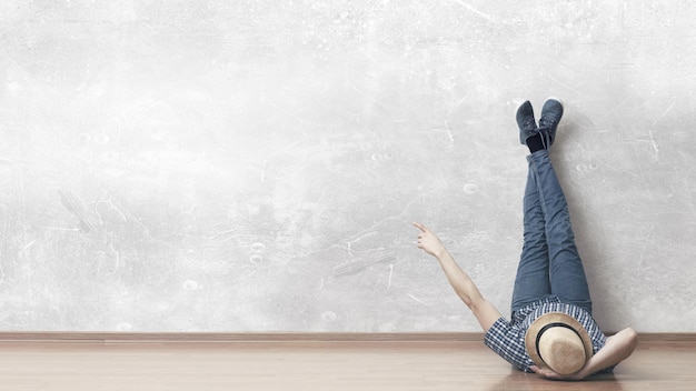 Young man in casual clothes and hat lying on the floor with legs raised up. Mixed media