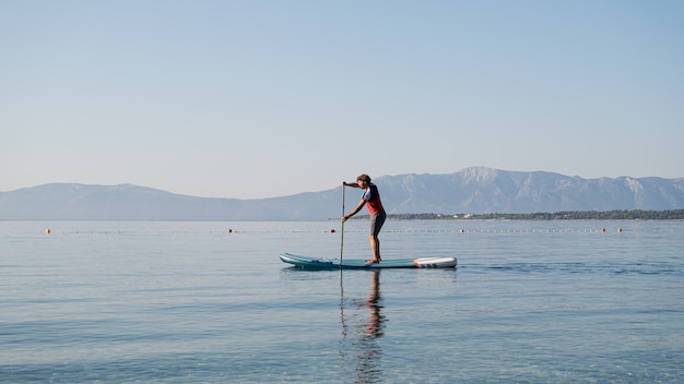 Photo young man in casual clothing paddling on sup board