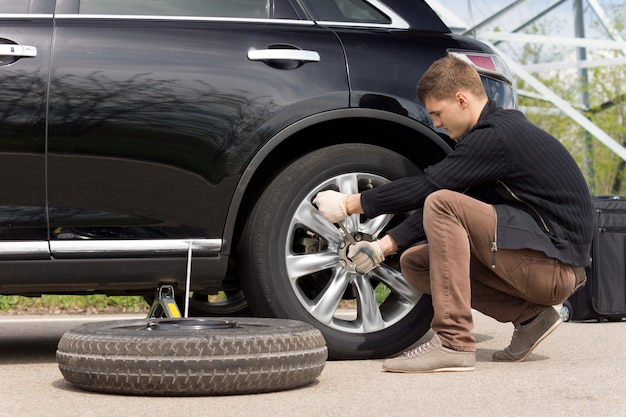 Young man changing the punctured tire on his car