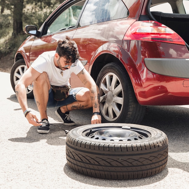 Young man changing the tire of broken down red car