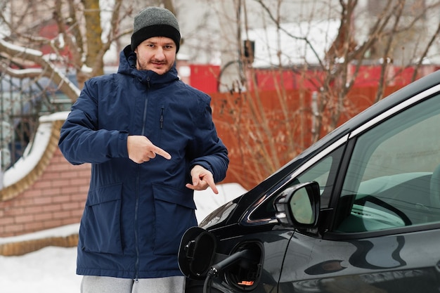 Young man charging his electric car in winter Eco transport concept