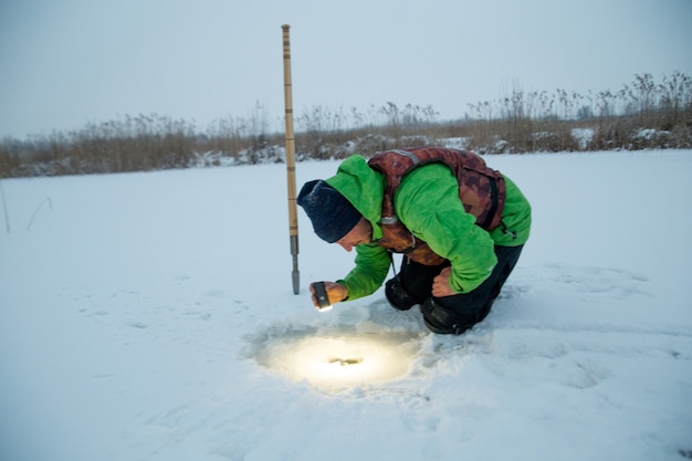 Young man checks a hole in a frozen lake on a winter fisherman