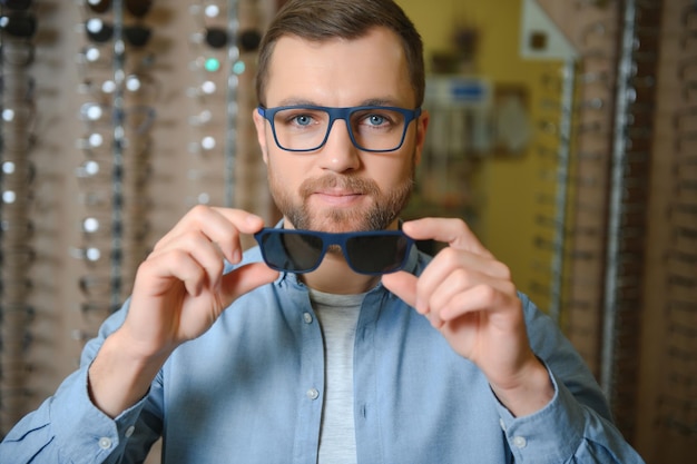 Young man choosing spectacles at optic shop