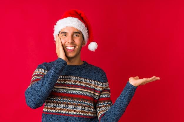 Young man on christmas day smiling and pointing aside, showing something at blank space.