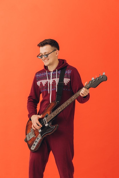 A young man in a Christmas kigurumi plays an electric guitar on a colored background