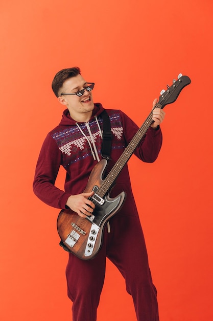 A young man in a Christmas kigurumi plays an electric guitar on a colored background