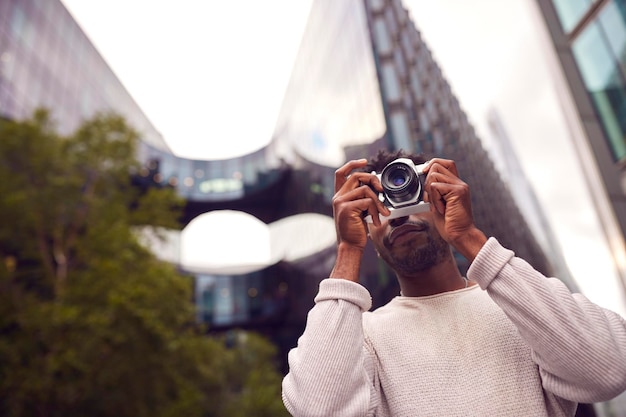 Young Man In City Taking Photo On Digital Camera To Post To Social Media