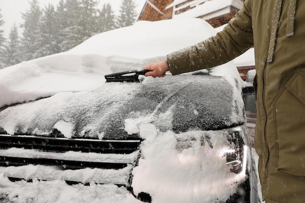 Young man cleaning snow from car outdoors on winter day closeup