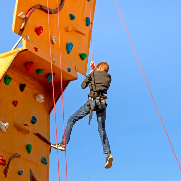 Young man climbing on a simulator against the sky