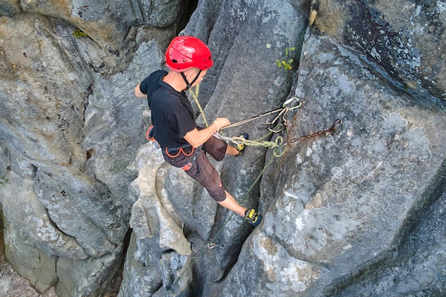 Young man climbing steep wall of rocky mountain Male climber overcomes challenging route Engaging in extreme sport concept