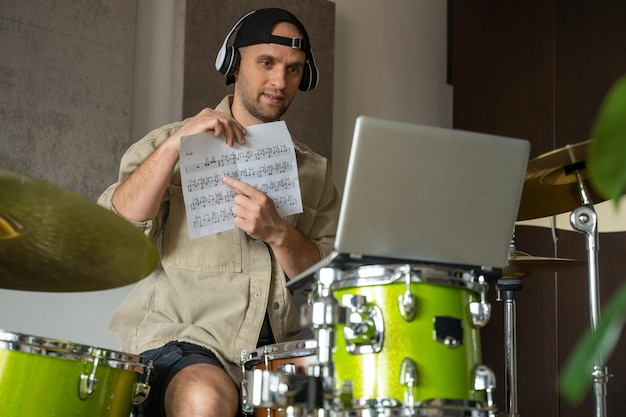 Young man conducts drum lesson via laptop guy starts lesson by greeting followers and shows music