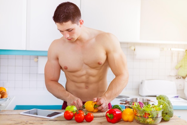 Young man cooking bodybuilder healthy meal vegetables tablet internet copyspace eating