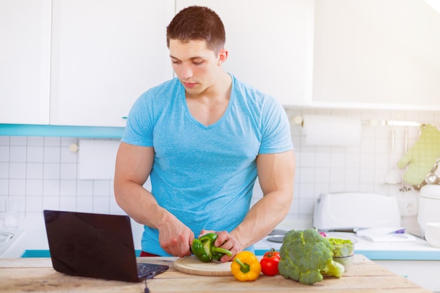 Young man cooking healthy meal vegetables computer internet eating