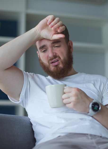 Young man coughing and suffering from cold drink hot beverage man feeling cold lying on the sofa