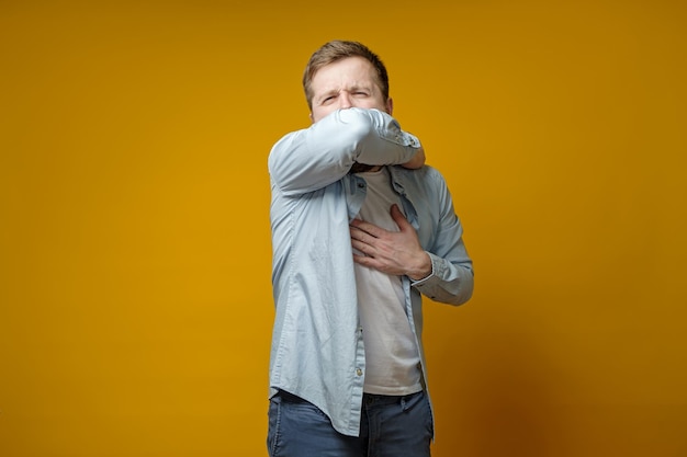 Young man coughs at his elbow and holds hand on chest experiencing pain Correct sneezing