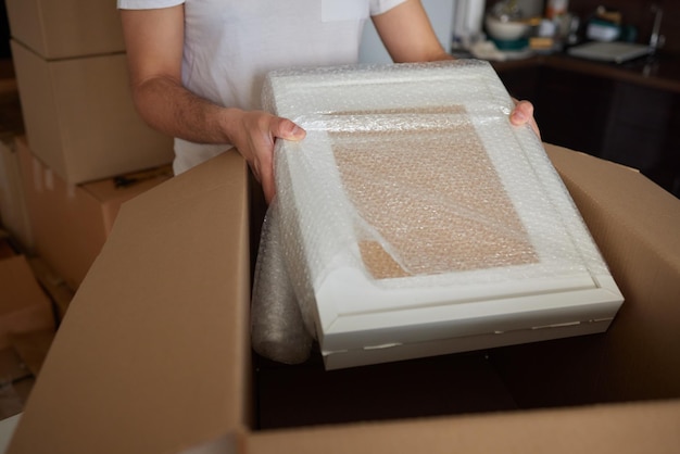 Photo a young man crouched down looking through a moving box filled with clothes books and a picture frame