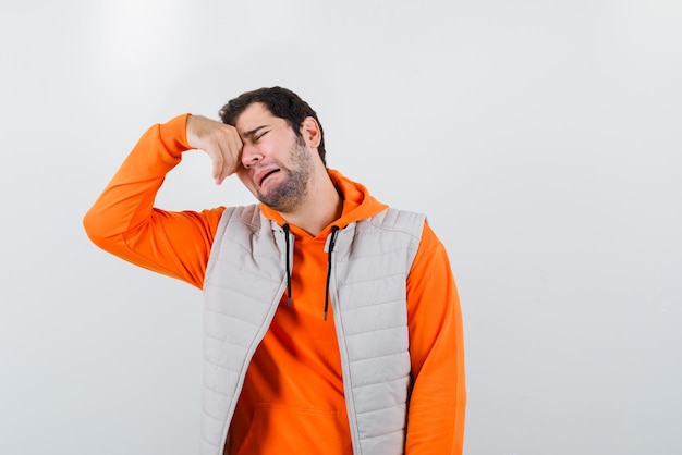 Young man crying and rubbing his eyes on white background