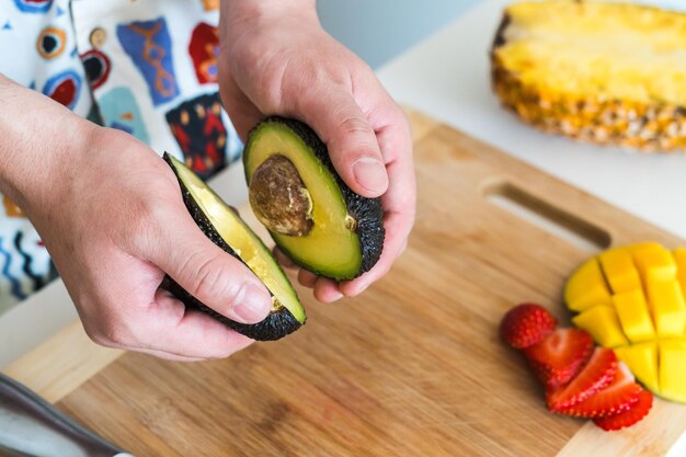 Photo young man cutting avocado while standing in kitchen at home