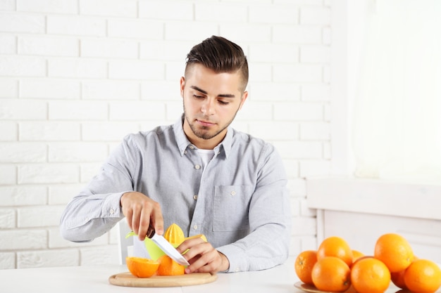 Young man cutting oranges, preparing orange juice