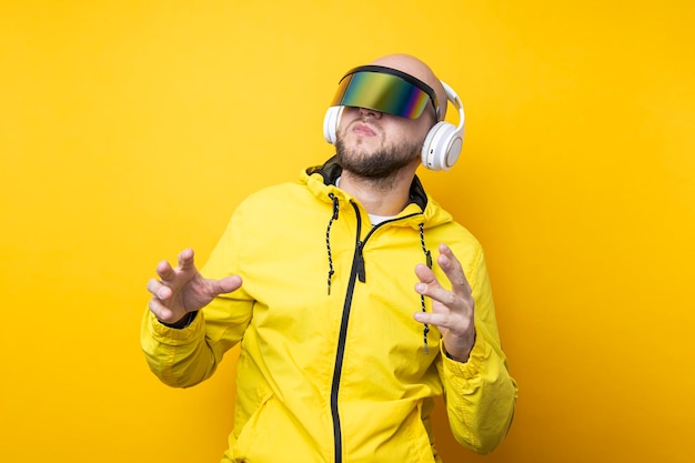 Young man in cyberpunk glasses in a yellow jacket with headphones dancing on a yellow background