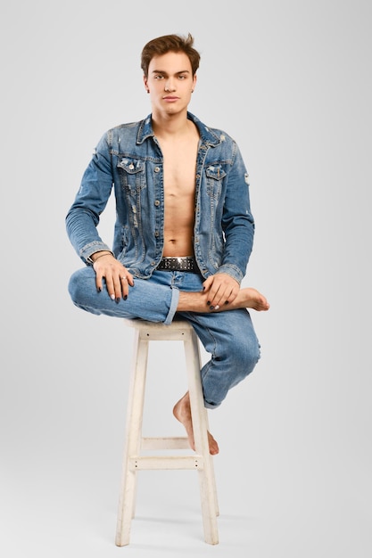 Young man in denim clothes sits on tall chair