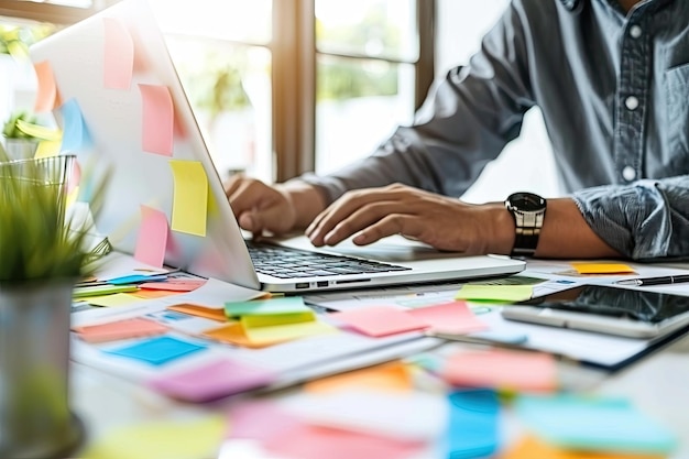 Young man at a desk with laptop surrounded by colorful sticky notes on a wall planning and organizing tasks