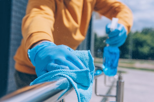 Young man disinfects a railing with a blue antiseptic and a rag in his hand