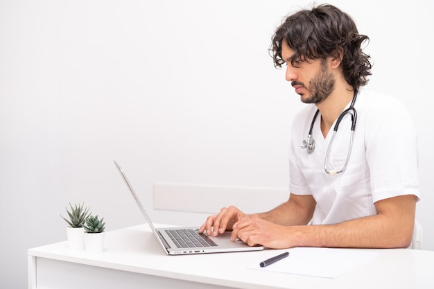 Young man doctor with stethoscope using computer laptop talking video conference call with patient at desk in health clinic Consulting and healthcare concept