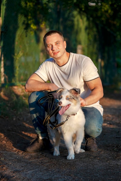 Young man and dog Aussie Australian Shepherd puppy in park on sunny day Concepts of friendship pets