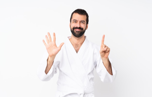 Young man doing karate over white counting six with fingers