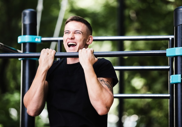 Young man doing pull ups on horizontal bar outdoors, workout, sport concept.