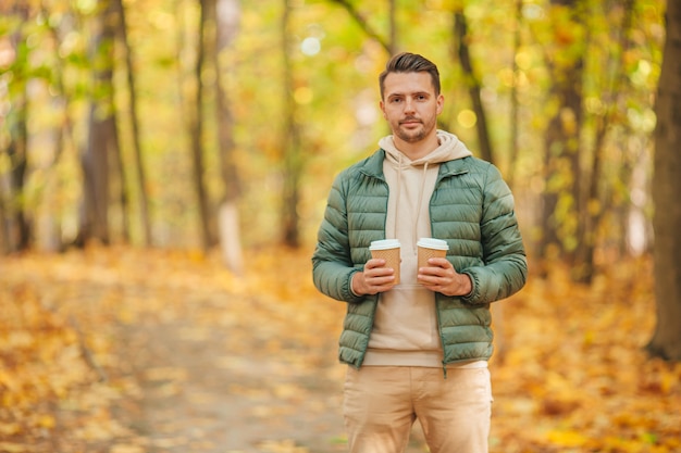 Young man drinking coffee in autumn park outdoors