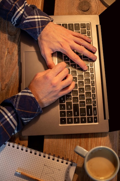 Young man drinking coffee in cafe and using laptop. Man's hands using laptop during coffee break