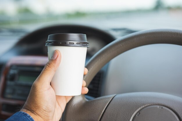 Young man drinking a cup of hot coffee while driving car to travel Hands holding steering wheel