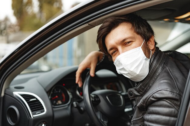 Young man driving car in medical mask