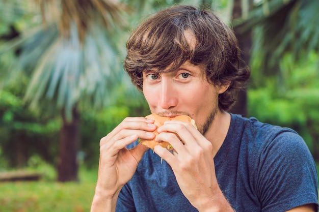 Young man eating a hamburger in the park.