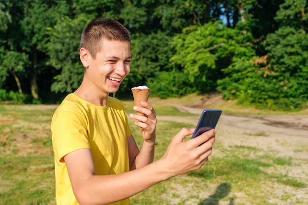 Young man eats ice cream and use smartphone outdoors