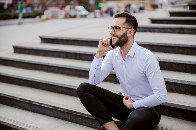 Young man elegantly dressed sitting on the stairs and having phone conversation.