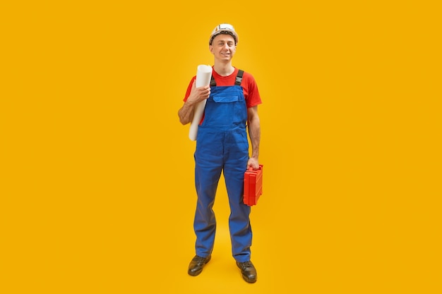 Young man engineer worker or architect with helmet holds documents blueprints and tool box Isolated on yellow background Copy space