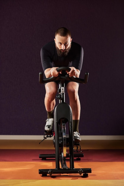 A young man on an exercise bike with a beard on a dark backgroundtraining on an exercise bike in the