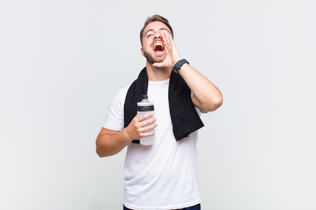 Young man feeling happy, excited and positive, giving a big shout out with hands next to mouth, calling out