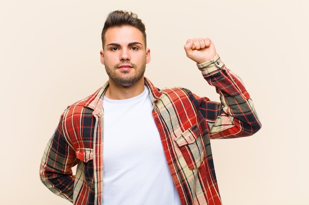 Young man feeling serious, strong and rebellious, raising fist up, protesting or fighting for revolution over isolated wall