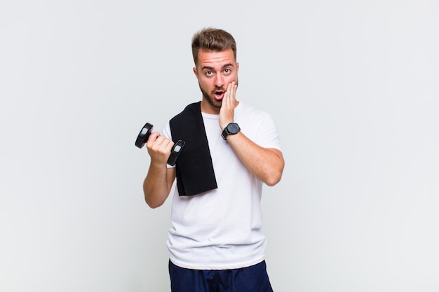 Young man feeling shocked and scared, looking terrified with open mouth and hands on cheeks