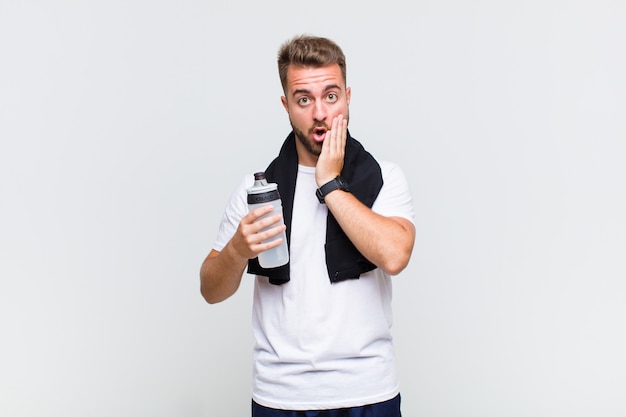 Young man feeling shocked and scared, looking terrified with open mouth and hands on cheeks