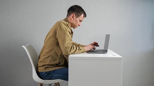 Young man fidgets on chair working via laptop at table