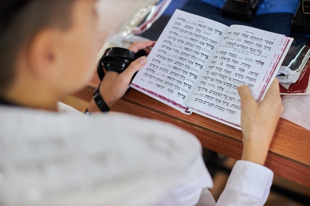 A young man finger pointing at a phrase in a bible book while reading a pray at a jewish ritual bar ...